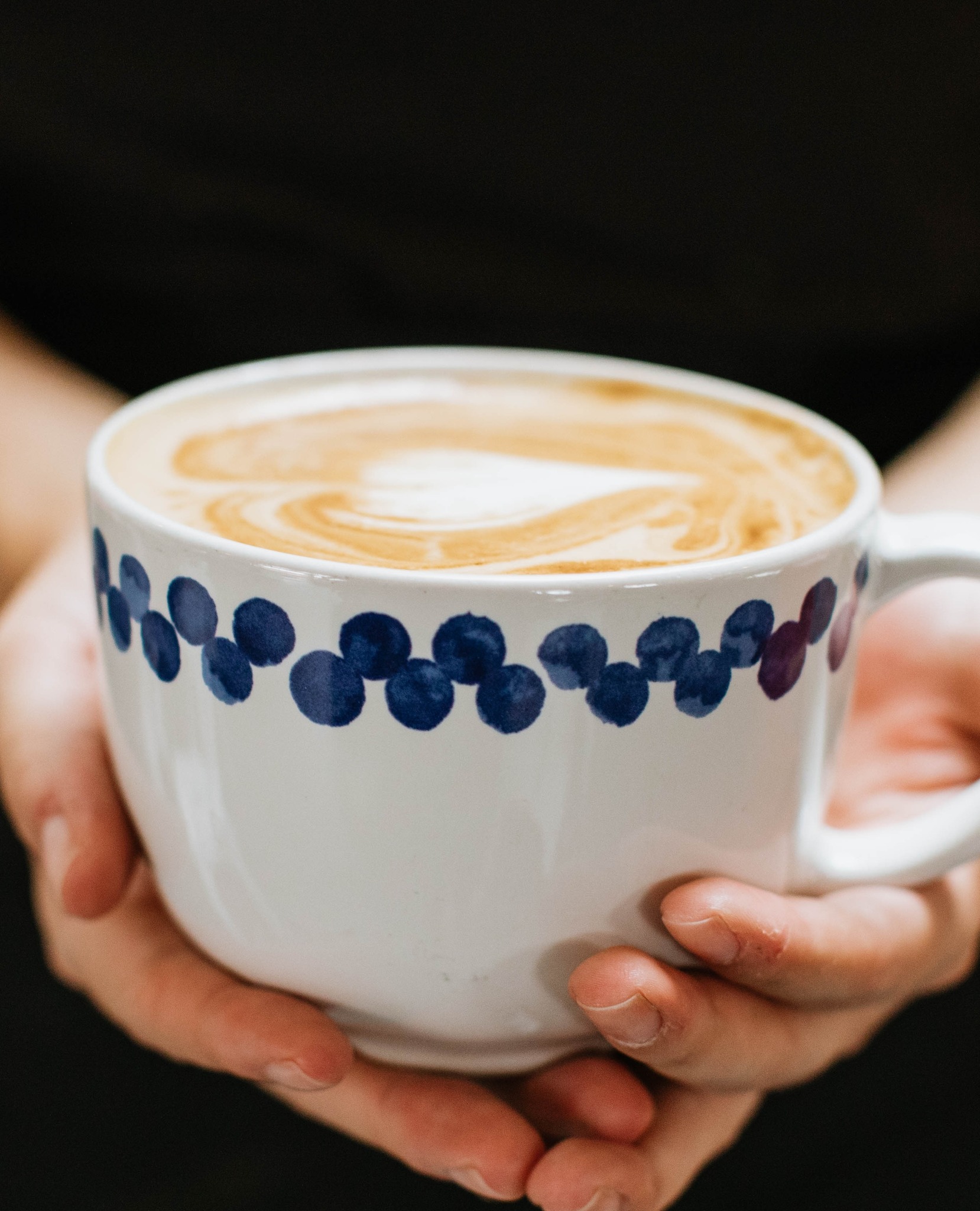 Two hands holding a latte in ceramic cup